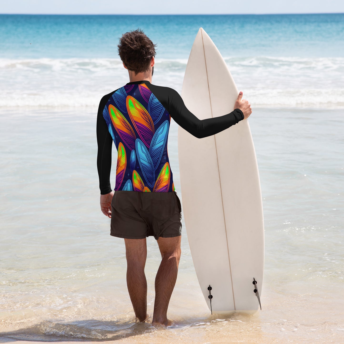 Man in colorful rash guard holding surfboard on beach, ready for surf adventure with UPF 50+ protection.