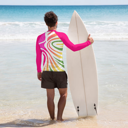 Man in a colorful abstract rash guard with pink sleeves, holding a surfboard at the beach, ready for an ocean adventure.