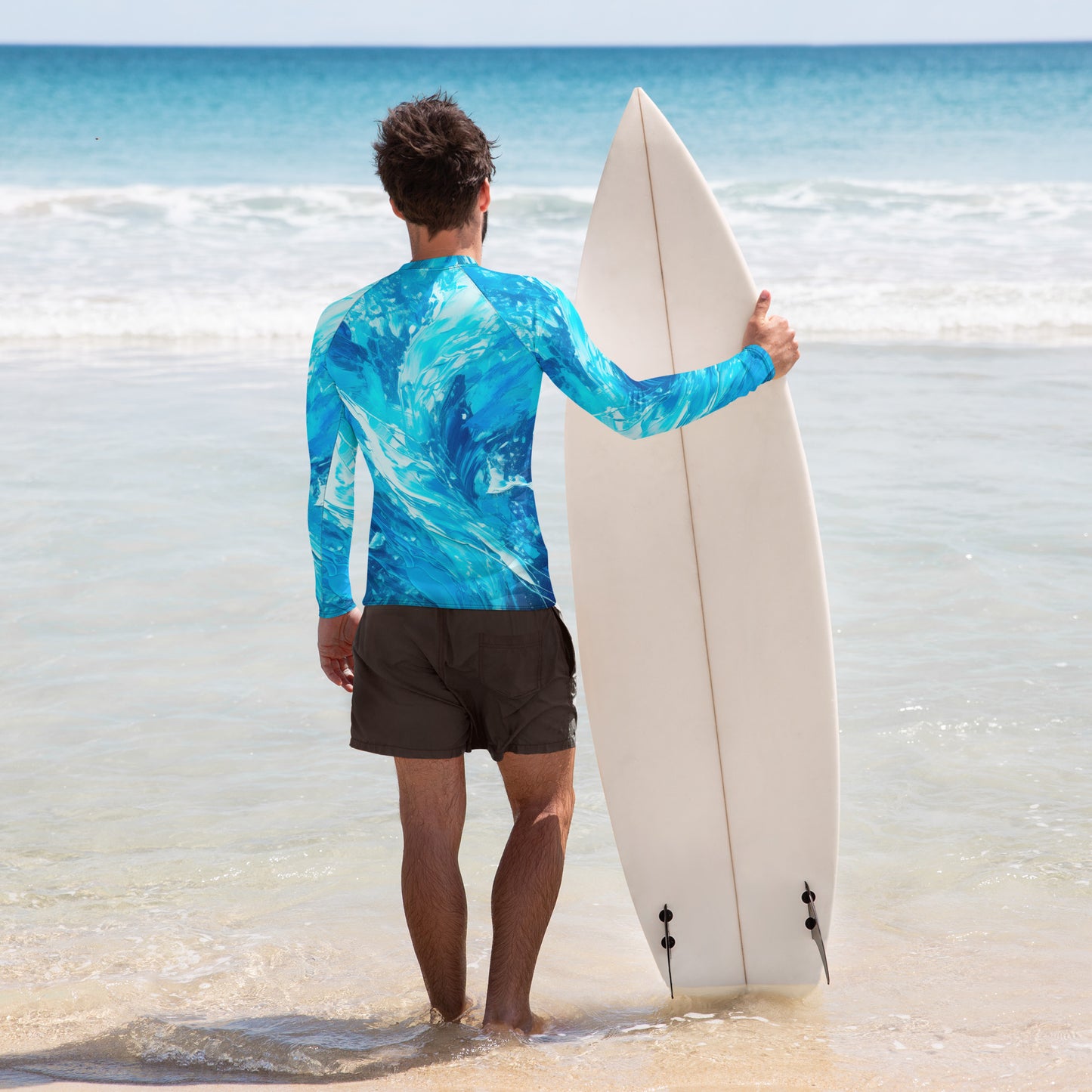 Man in a wave-pattern rash guard holding a surfboard on the beach, ready to ride the waves.