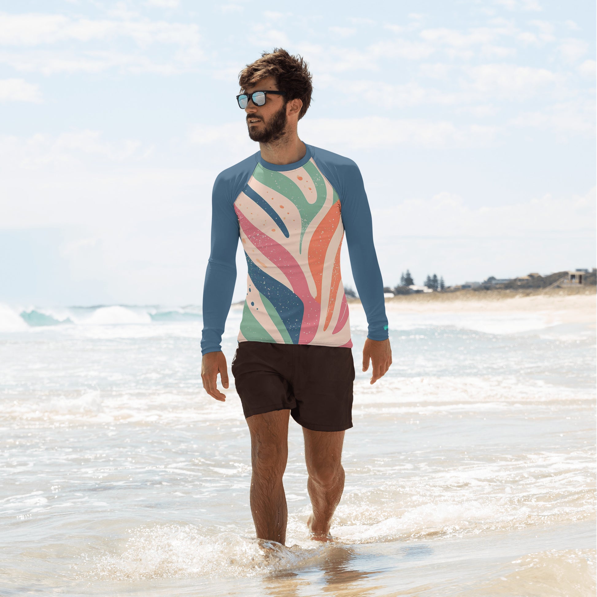 Man wearing a coral abstract Men's Rash Guard with UPF 50+ walking on the beach, enjoying sun protection in style.